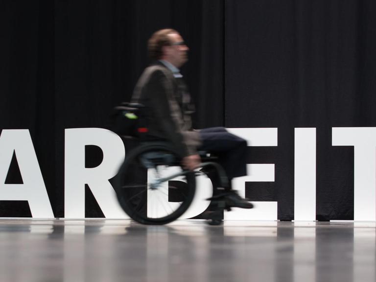 Ein Mensch mit Behinderung fährt am 20.02.2017 in Bielefeld mit seinem Rollstuhl an dem aufgestellten Wort "Arbeit" entlang.