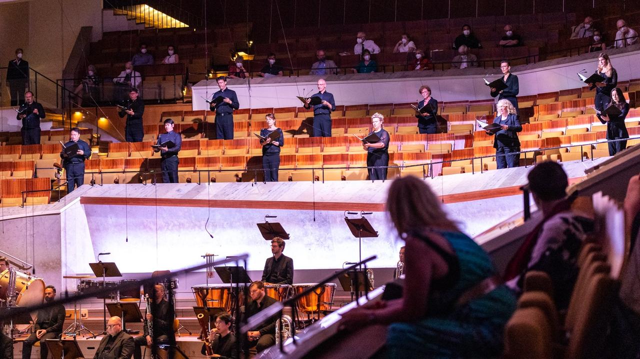 Sänger stehen auf den Rängen, denen das Publikum in der Philharmonie gespannt zuhört.
