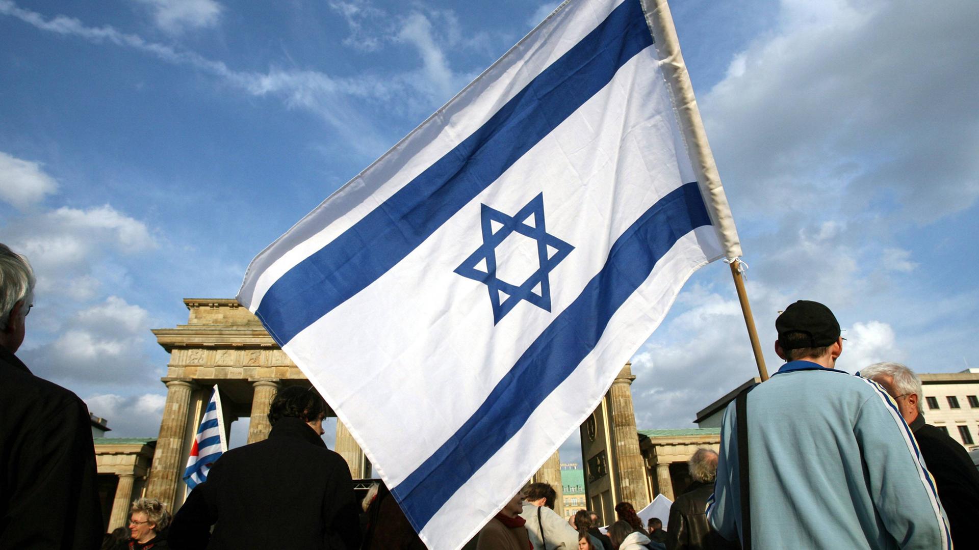 Ein Mann mit einer israelischen Fahne steht in Berlin am Brandenburger Tor.