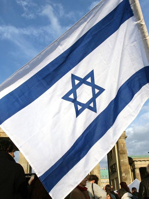 Ein Mann mit einer israelischen Fahne steht in Berlin am Brandenburger Tor.