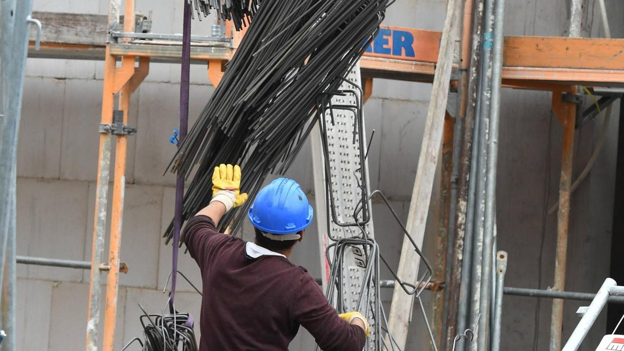 Ein Bauarbeiter bei der Arbeit auf der Baustelle. Er trägt einen Helm und steht mit dem Rücken zur Kamera. 