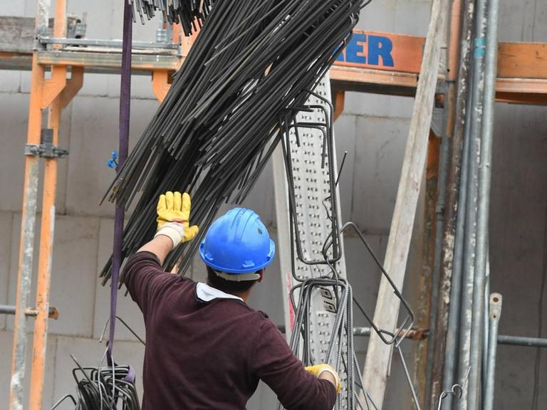 Ein Bauarbeiter bei der Arbeit auf der Baustelle. Er trägt einen Helm und steht mit dem Rücken zur Kamera. 