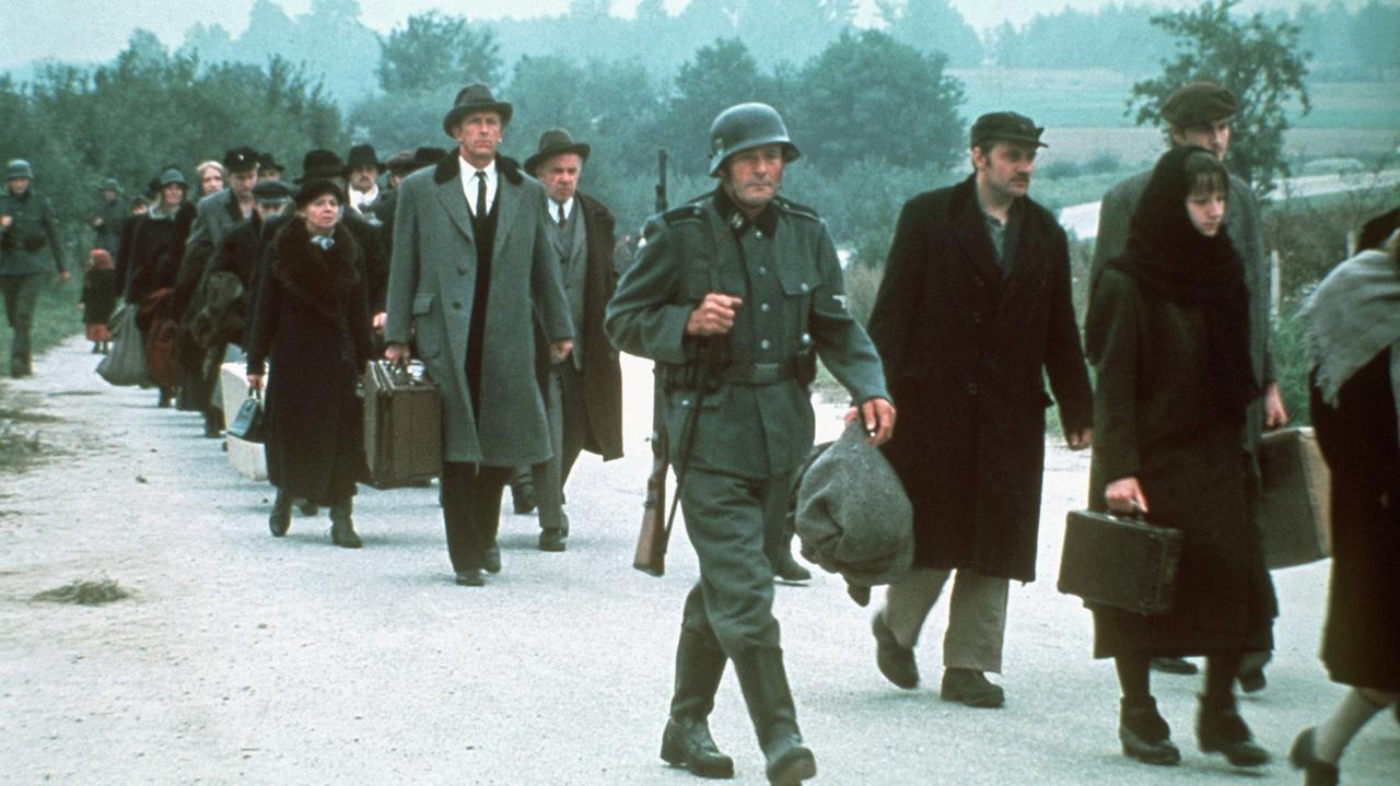 Das Bild zeigt eine Szene aus der US-amerikanischen Fernsehserie "Holocaust", in der deportierte Juden auf dem Weg ins Konzentrationslager durch den Schnee gehen.