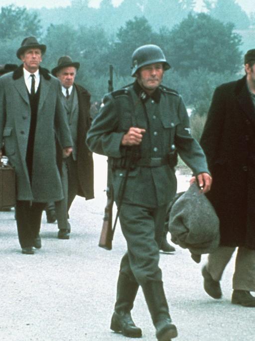 Das Bild zeigt eine Szene aus der US-amerikanischen Fernsehserie "Holocaust", in der deportierte Juden auf dem Weg ins Konzentrationslager durch den Schnee gehen.