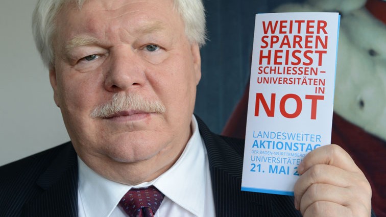 Horst Hippler hält ein Faltblatt mit der Aufschrift "Weiter sparen heißt schließen - Universitäten in Not" hoch. 