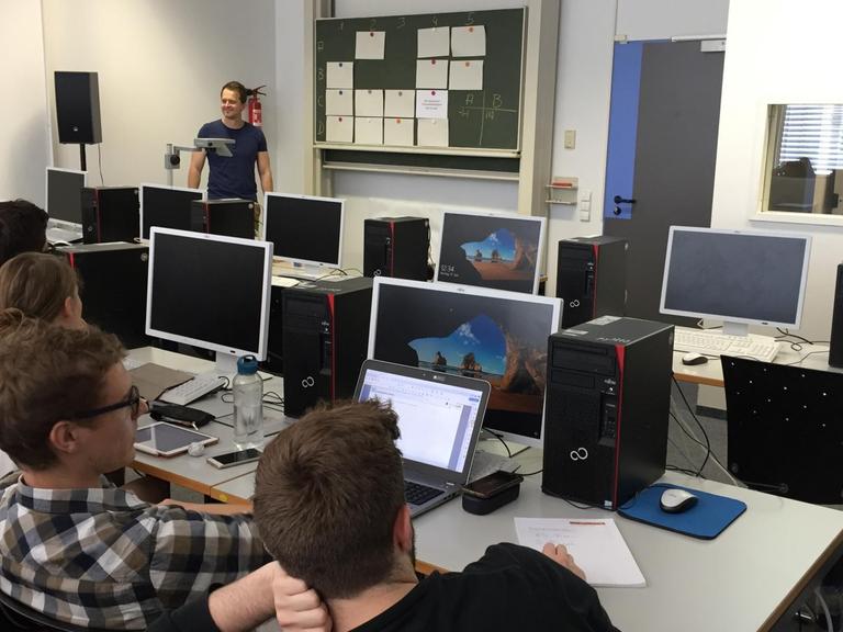 Der Dozent Dr. Stefan Fedtke steht im Computerraum und bespricht mit Studierenden ein Simulationsprojekt