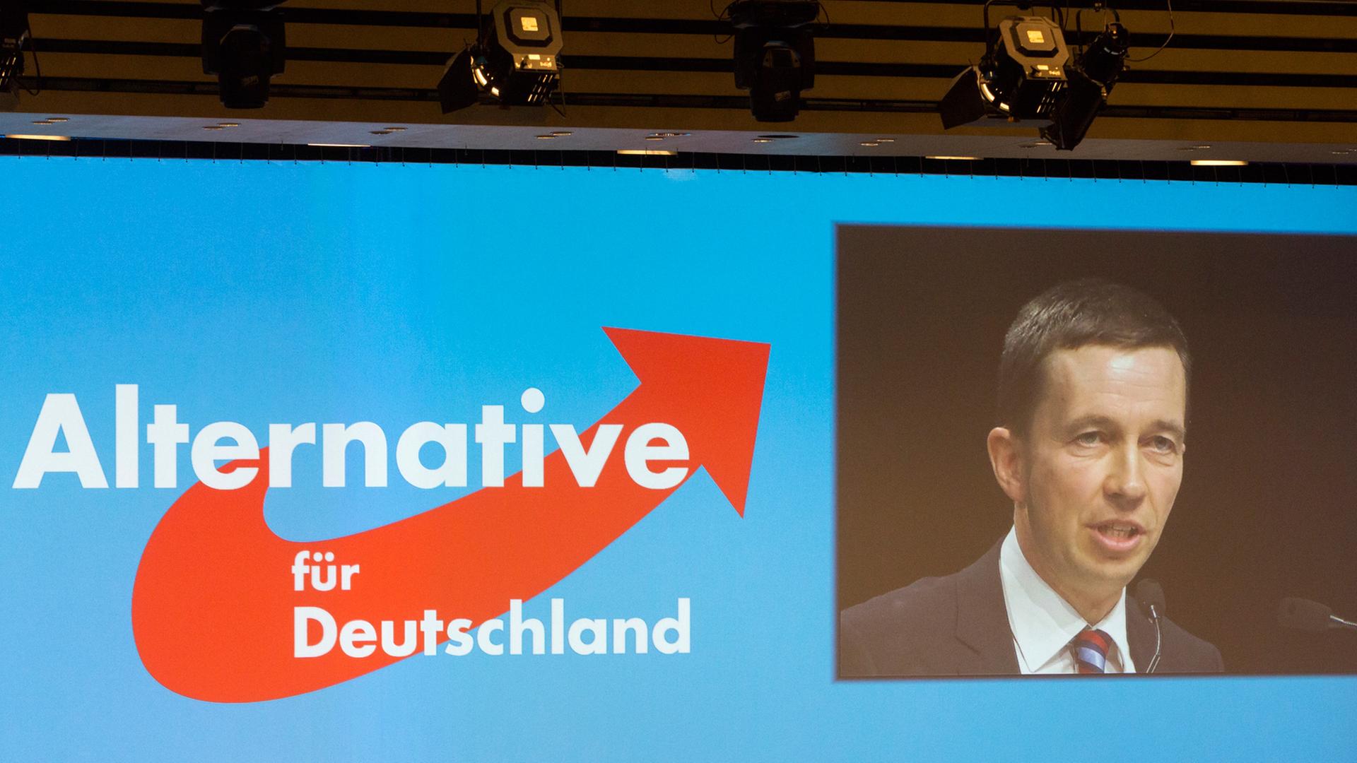 Leinwand mit dem Logo der AfD und einem Bild der Videoübertragung der Rede von Bernd Lucke.