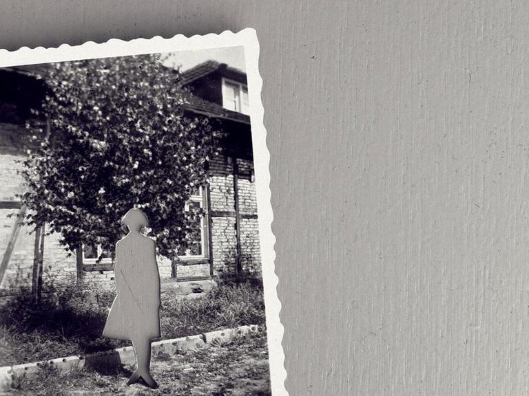 Auf einer grauen Fläche liegt eine alte schwarz weiss Fotografie, mit einer aus dem Foto herausgeschnittenen Person.