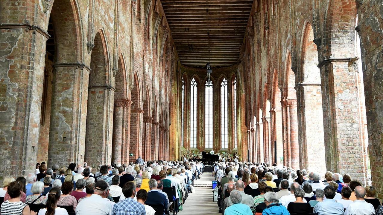 Viele Besucher sitzen am 25.06.2016 in Chorin (Brandenburg) bei Regenschauern während des Eröffnungskonzertes des Choriner Musiksommers in der Klosterruine