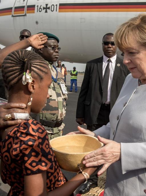 Bundeskanzlerin Angela Merkel (CDU) wird am 09.10.2016 in Bamako in Mali neben Staatspräsident Ibrahim Boubacar Keita (r) am Flughafen von Blumenmädchen begrüßt, die der Kanzlerin zunächst eine traditionelle Wasserkalebasse reichen.