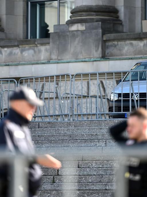 Drei Polizisten stehen mit Absperrgittern vor dem Reichstagsgebäude in Berlin.