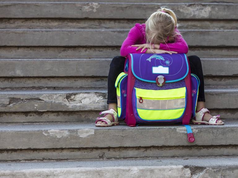 Ein trauriges Mädchen sitzt auf einer Treppe.