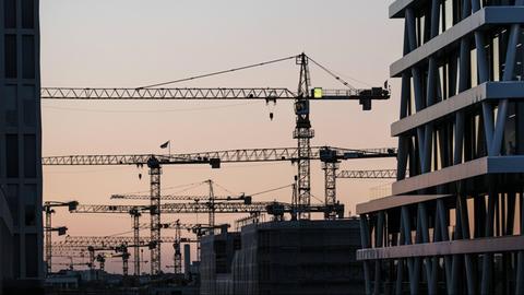 Kräne stehen zwischen Hausfassaden in Berlin.