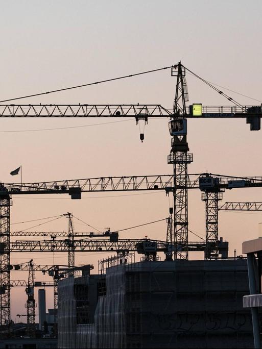 Kräne stehen zwischen Hausfassaden in Berlin.
