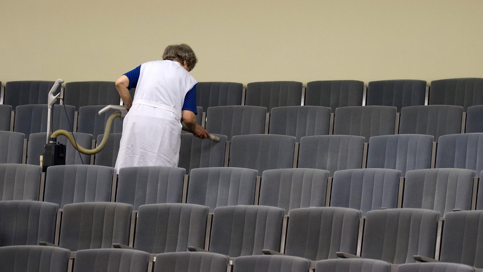 Eine Frau saugt Stühle in einem Theater ab.
