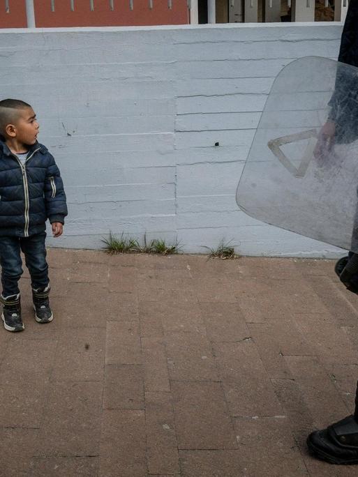 Ein kleiner Junge steht im Hafen der griechischen Insel Lesbos vor einem Polizisten
