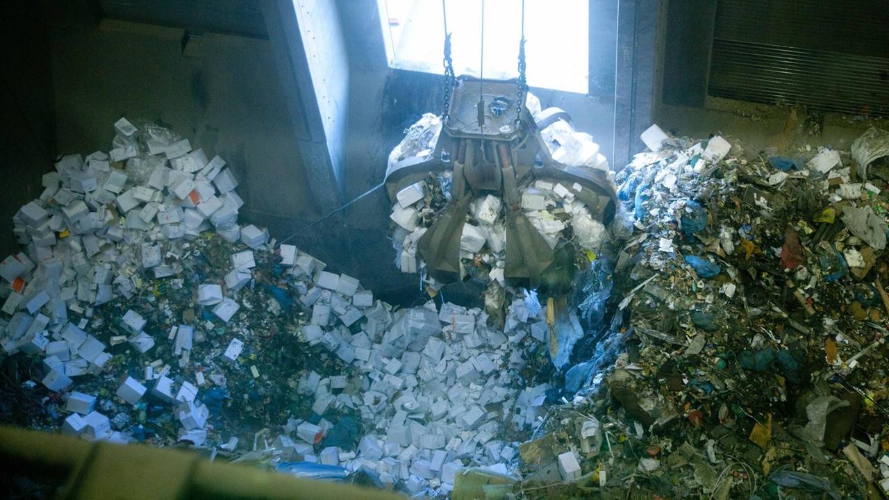 Eine Greifzange greift in einen großen Haufen Verpackungen in einer Müllanlage