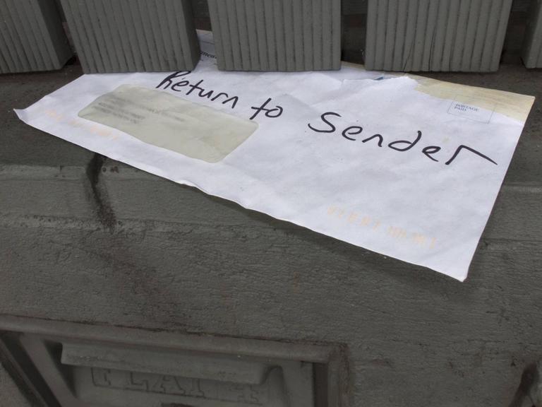Ein weisser Briefumschlag steckt in einer Tür: "Return to sender" steht darauf.