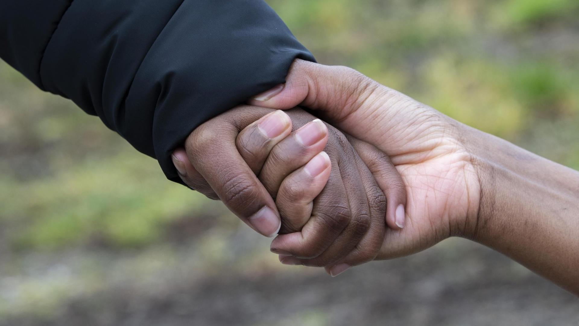 Die Hand einer erwachsenen schwarzen Frau und eines schwarzen Kindes halten sich