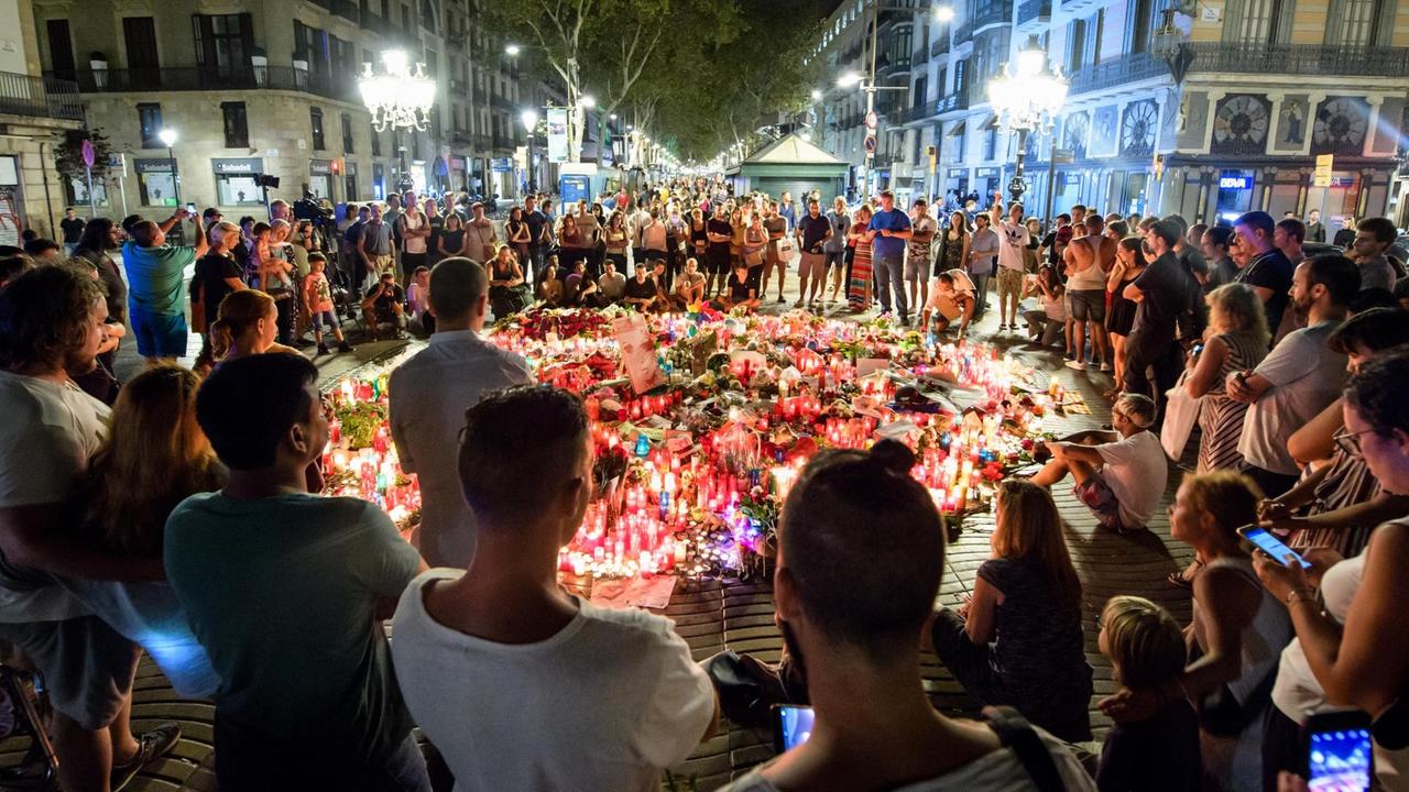 Zahlreiche Menschen stehen am 19.08.2017 auf der Flaniermeile Las Ramblas in Barcelona (Spanien) im Kreis um niedergelegte Blumen und Kerzen. 
