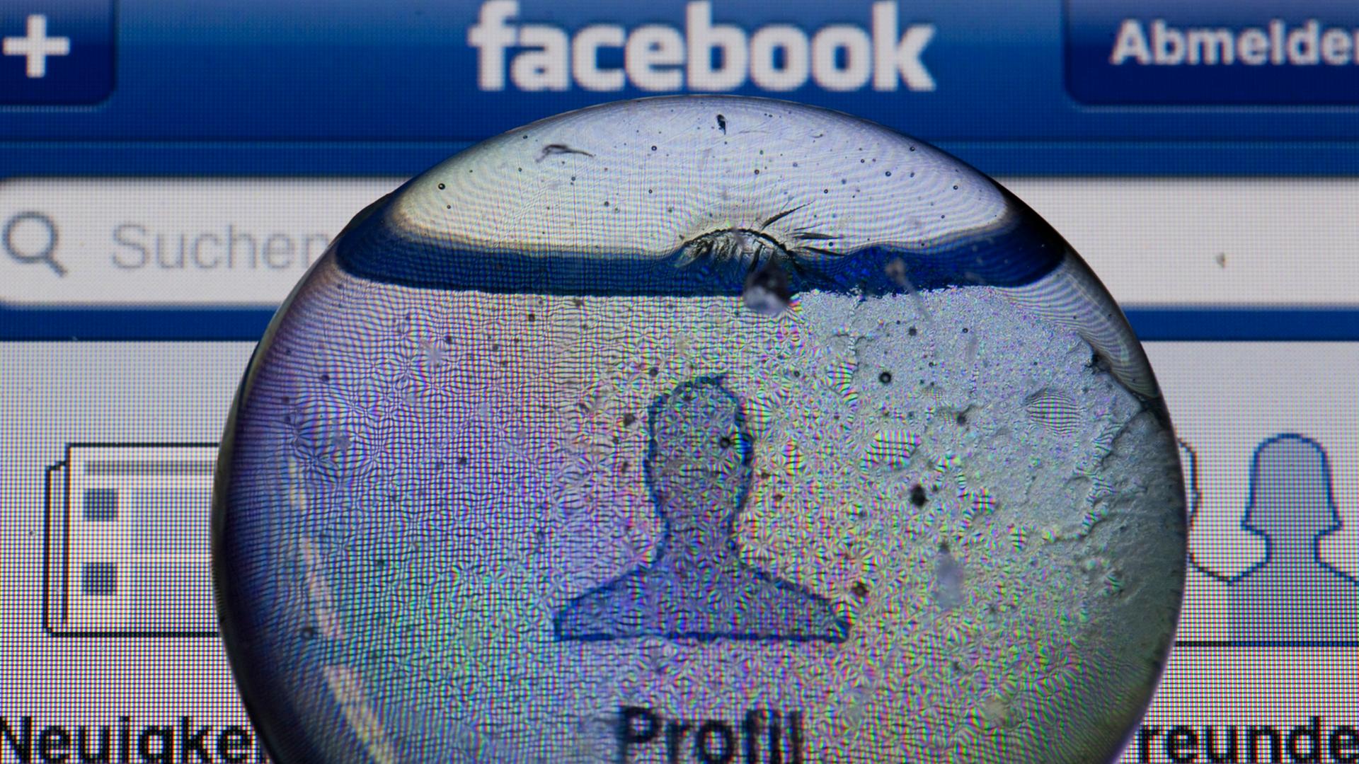 Ein Glasstein liegt auf dem Bildschirm eines iPhones und vergrößert das Profil-Icon einer Facebook-Anwendung.