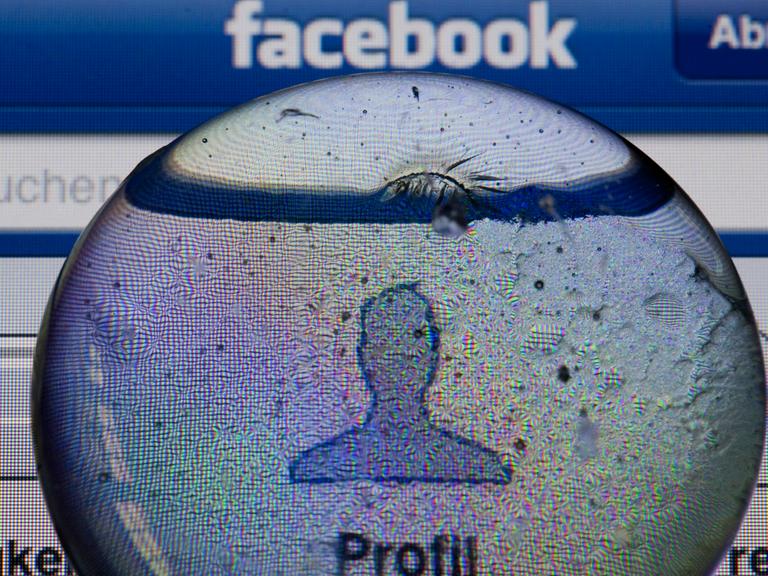Ein Glasstein liegt auf dem Bildschirm eines iPhones und vergrößert das Profil-Icon einer Facebook-Anwendung.