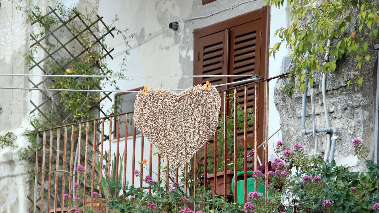 Eine herzförmige Fußmatte hängt an einer Wäscheleine vor dem Balkon eines Hauses in Matera
