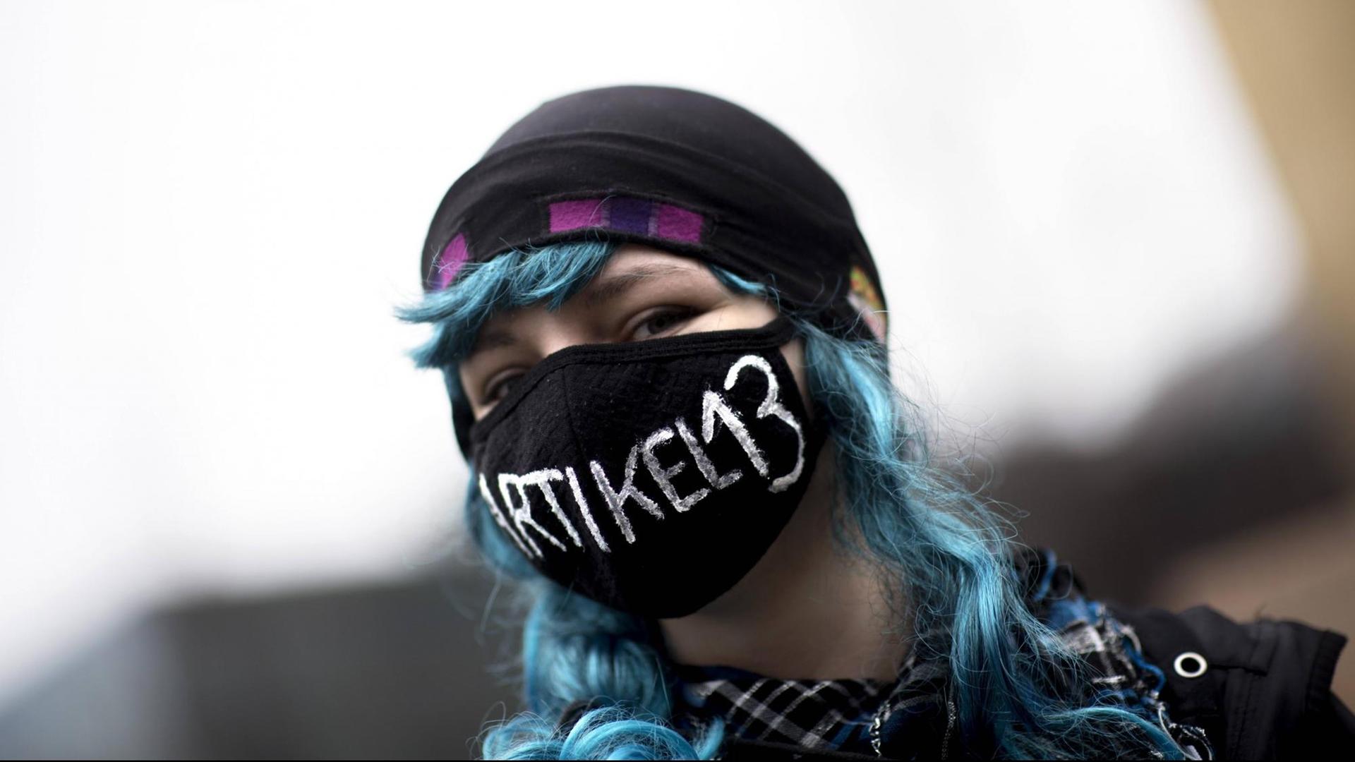 Eine junge Demonstrantin protestiert in Berlin gegen die EU-Urheberrechtsreform. Sie trägt einen Mundschutz, auf dem "Artikel 13" steht.