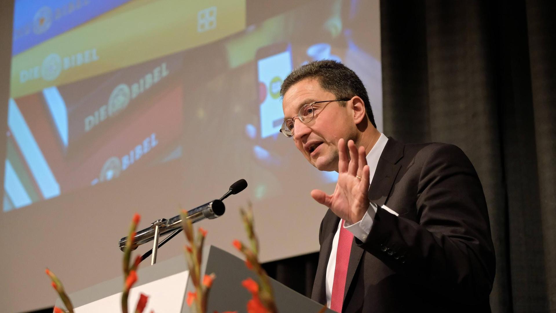 Alexander Deeg steht an einem Redepult hält einen Vortrag. Im Hintergrund ist ein an die Wand projiziertes Bild zu sehen.