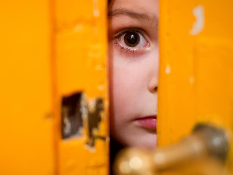 Ein junges Mädchen schaut am 24.01.2014 in Berlin durch einen Türschlitz.