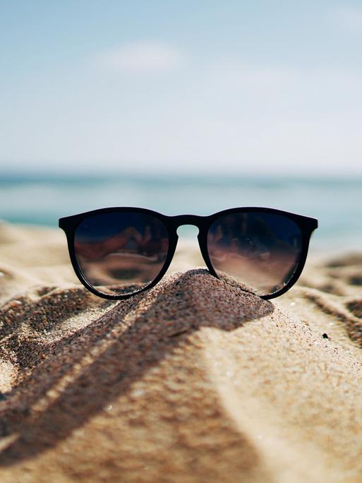 Eine Sonnenbrille liegt im Sand an einem Strand.