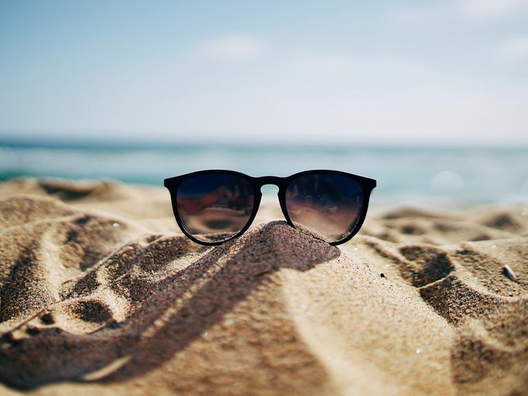 Eine Sonnenbrille liegt im Sand an einem Strand.