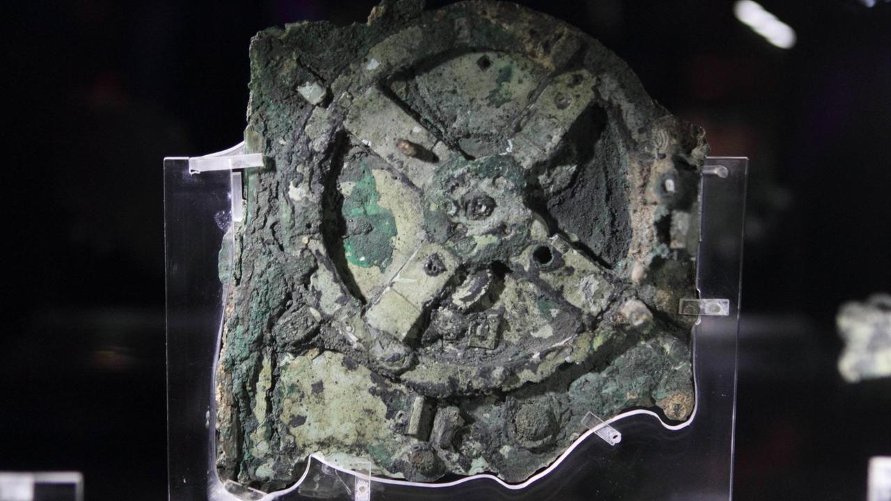 Der Mechanismus von Antikythera, ein nicht mehr funktionierendes, unvollständig erhaltenes Fundstück mit 82 Fragmenten aus der Antike mit einer Vielzahl von Zahnrädern in ähnlicher Anordnung wie in einer Räderuhr, im Archäologischen Nationalmuseum Athen