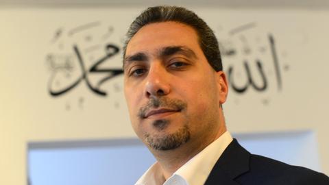 Porträt von Sadiqu Al-Mousllie, aufgenommen im April 2014 in der Iqra-Moschee in Braunschweig. Der Schriftzug im Hintergrund bedeutet "Allah, der Erhabene" und "Mohammed, Friede sei mit ihm".