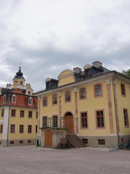 Ein barockes Schloß mit gelbem Anstrich und Treppenaufgang und Nebengebäude links.