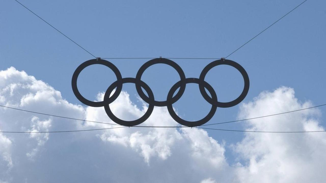 Die olympischen Ringe vor einem blauen Himmel. Im Hintergrund große weiße Wolken.