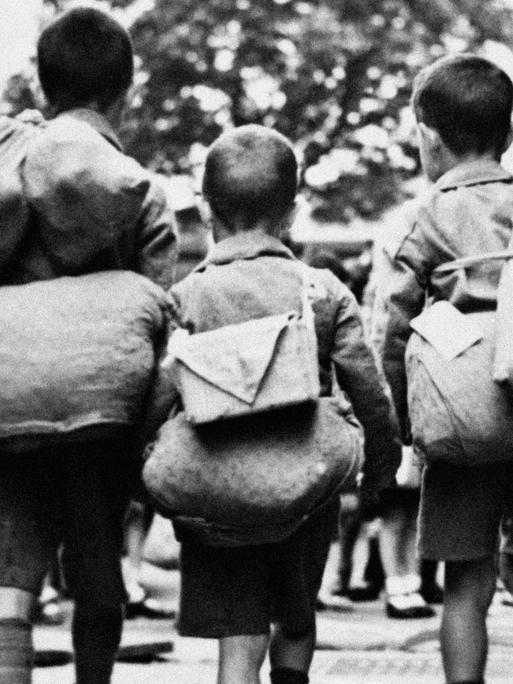 Kinderverschickung: undatierte historische Aufnahme von drei Kindern mit Gepäck auf dem Rücken.