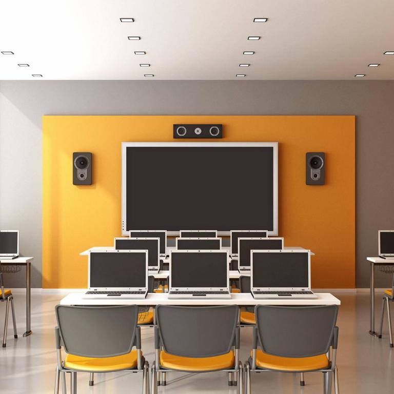 In einem Unterrichtsraum mit einer digitalen Tafel stehen Tischreihen mit Laptops
