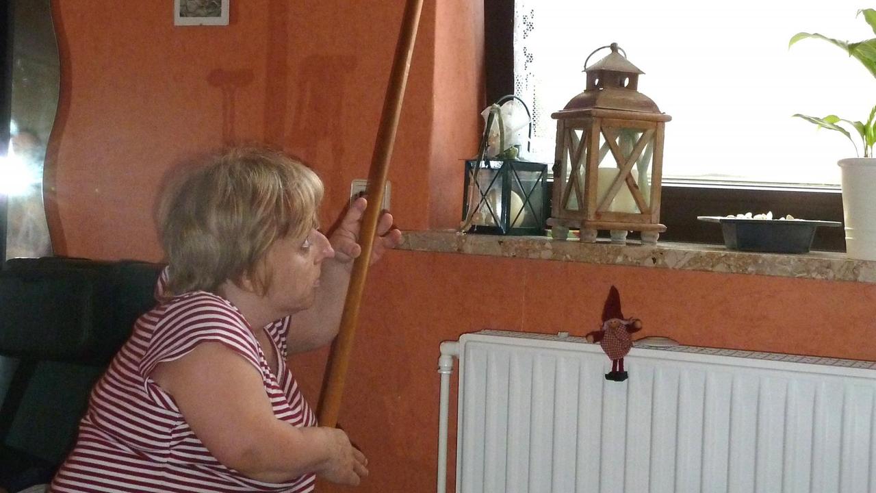  Eine kleine Frau öffnet und schließt mithilfe eines Stockes ein Fenster. 