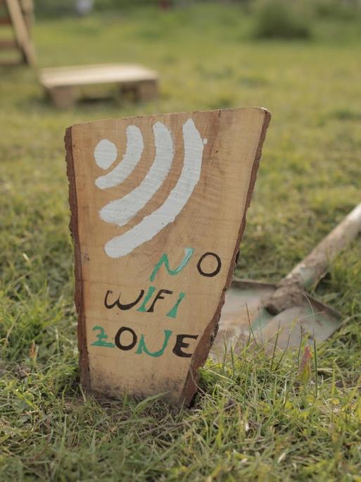 Auf einem Holzbrett steht „No Wifi Zon“ — dahinter liegt ein Spaten.
