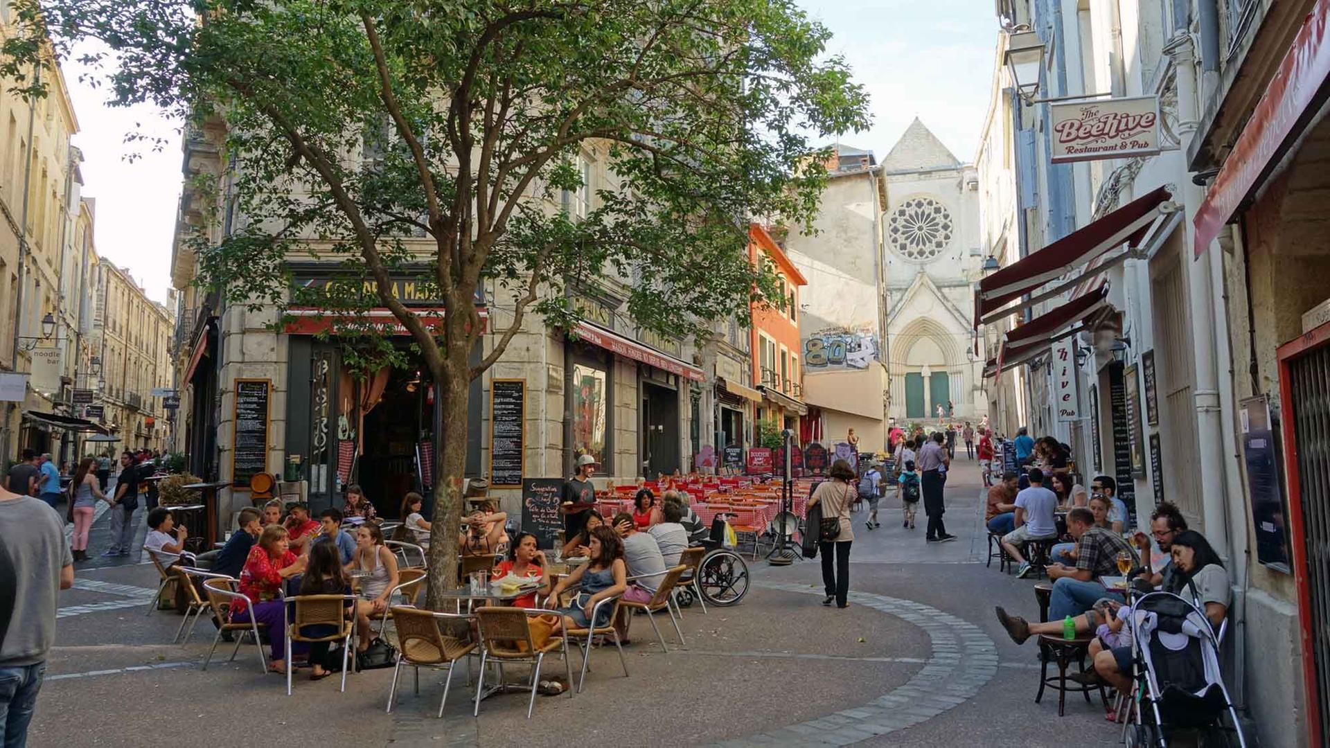 Menschen sitzen vor zahlreichen Cafés und Bars in der Altstadt von Montpellier.