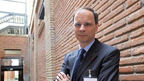 Jean Tirole steht, die Arme verschränkt, vor einer Mauer.