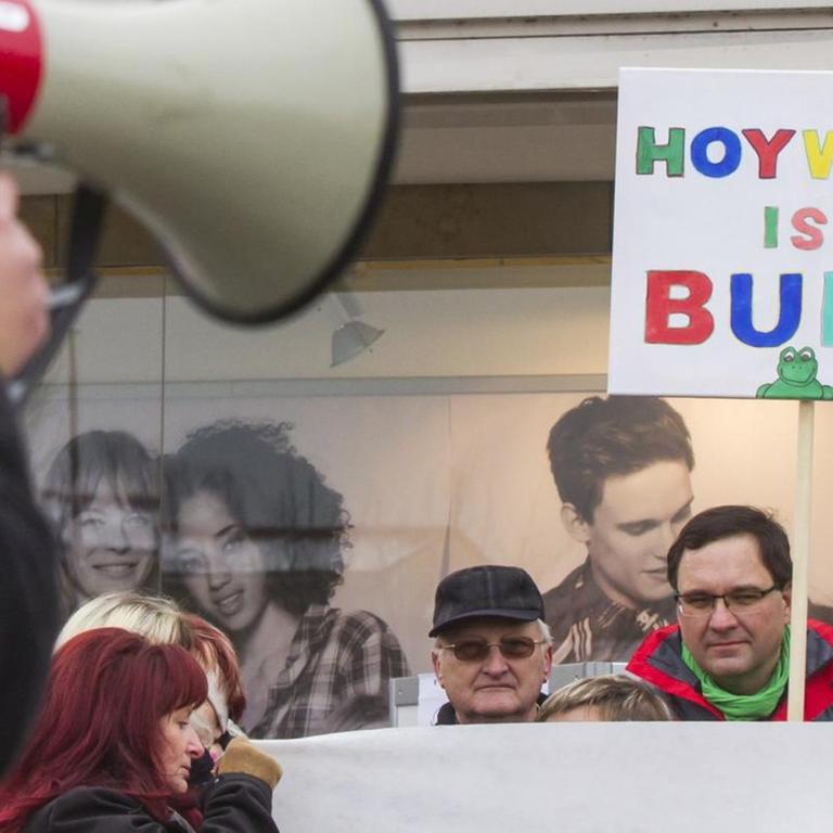 Auf einem Platz stehe mit Menschen mit einem Schild,  auf dem steht "Hoywoy ist bunt".