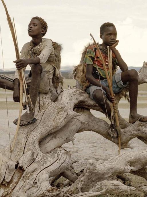 Am Eyasi-See in Tansania halten Osama (15) und Manu (14) Pfeil und Bogen in der Hand, während sie auf einem abgestorbenen Baum sitzen. Sie gehören den Hadza an, einer der letzten Gemeinschaften von Jägern und Sammlern.
