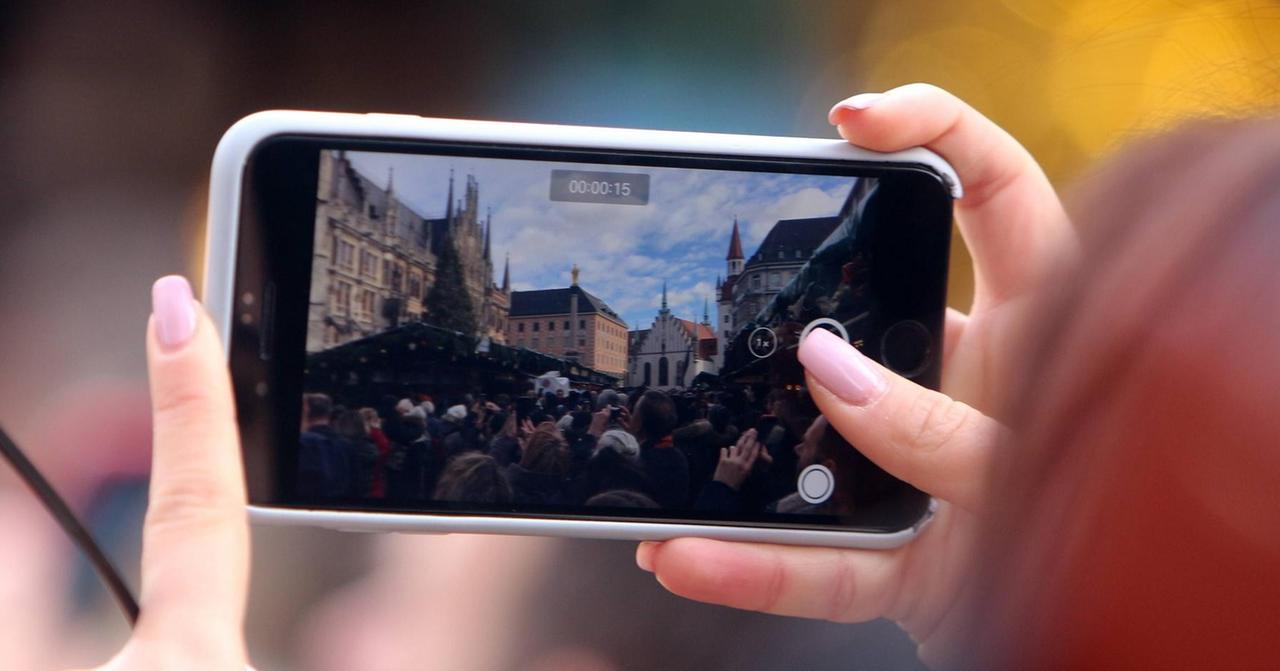 Besucherin filmt mit ihrem Smartphone den Christkindlmarkt auf dem Marienplatz am Rathaus in München, Bayern, Deutschland