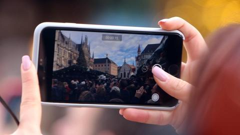 Besucherin filmt mit ihrem Smartphone den Christkindlmarkt auf dem Marienplatz am Rathaus in München, Bayern, Deutschland