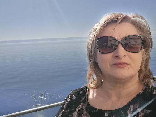 Eine Frau mit Sonnenbrille. Im Hintergrund ist das Wasser eines großen Sees zu sehen.