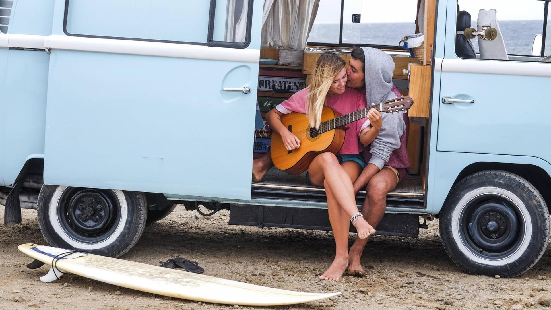 Ein Paar sitzt an einem Transporter und spielt Gitarre