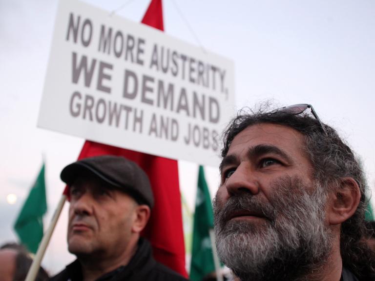 Zwei Demonstranten, im Hintergrund ein Plakat mit der Aufschrift: "No more austerity, we demand jobs and growth"