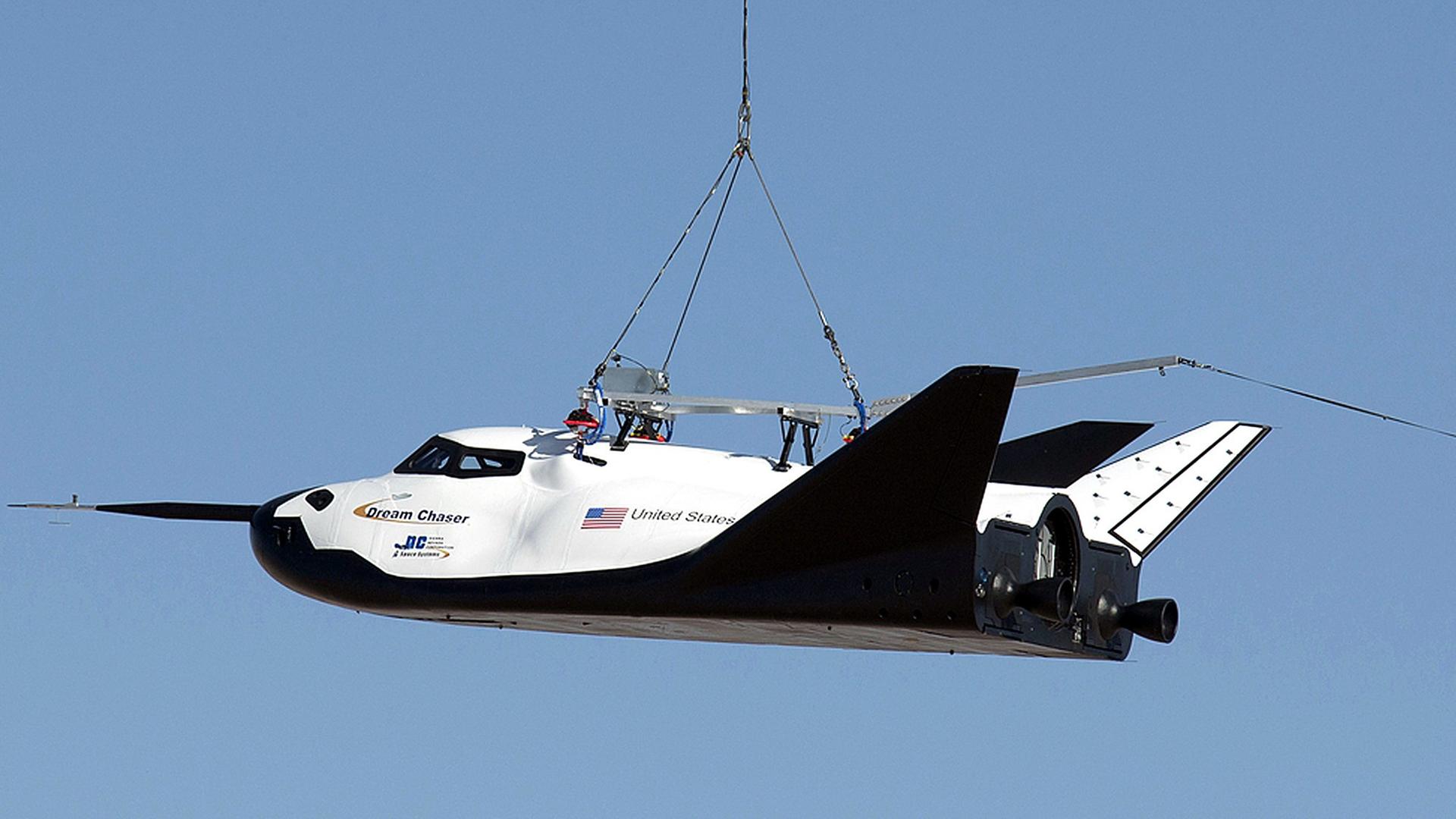 Ein Hubschrauber trägt den Mini-Shuttle Dream Chaser an einem Seil.